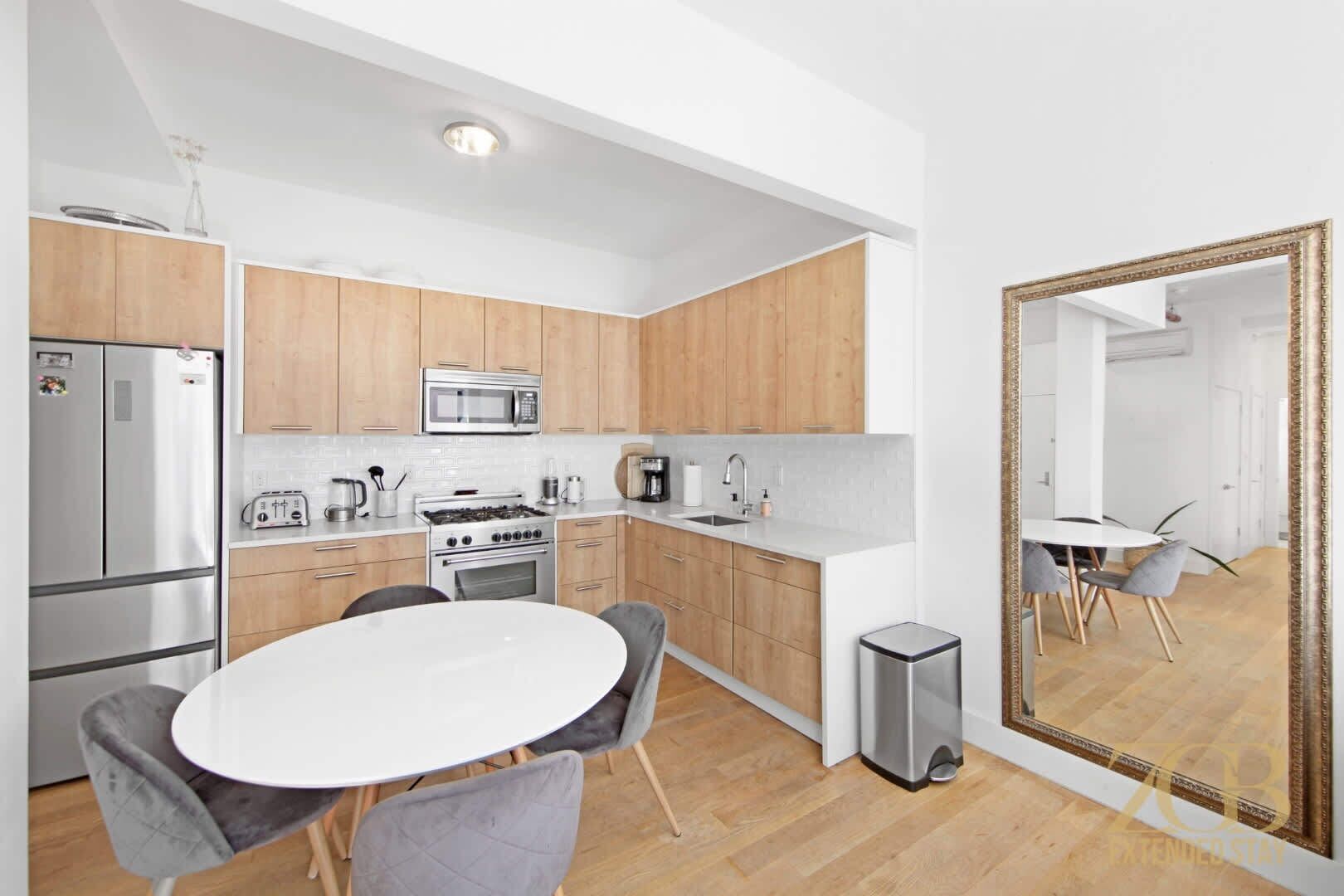 Une cuisine moderne avec des meubles en bois, des appareils en acier inoxydable et une table de salle à manger ronde, accompagnée de chaises.