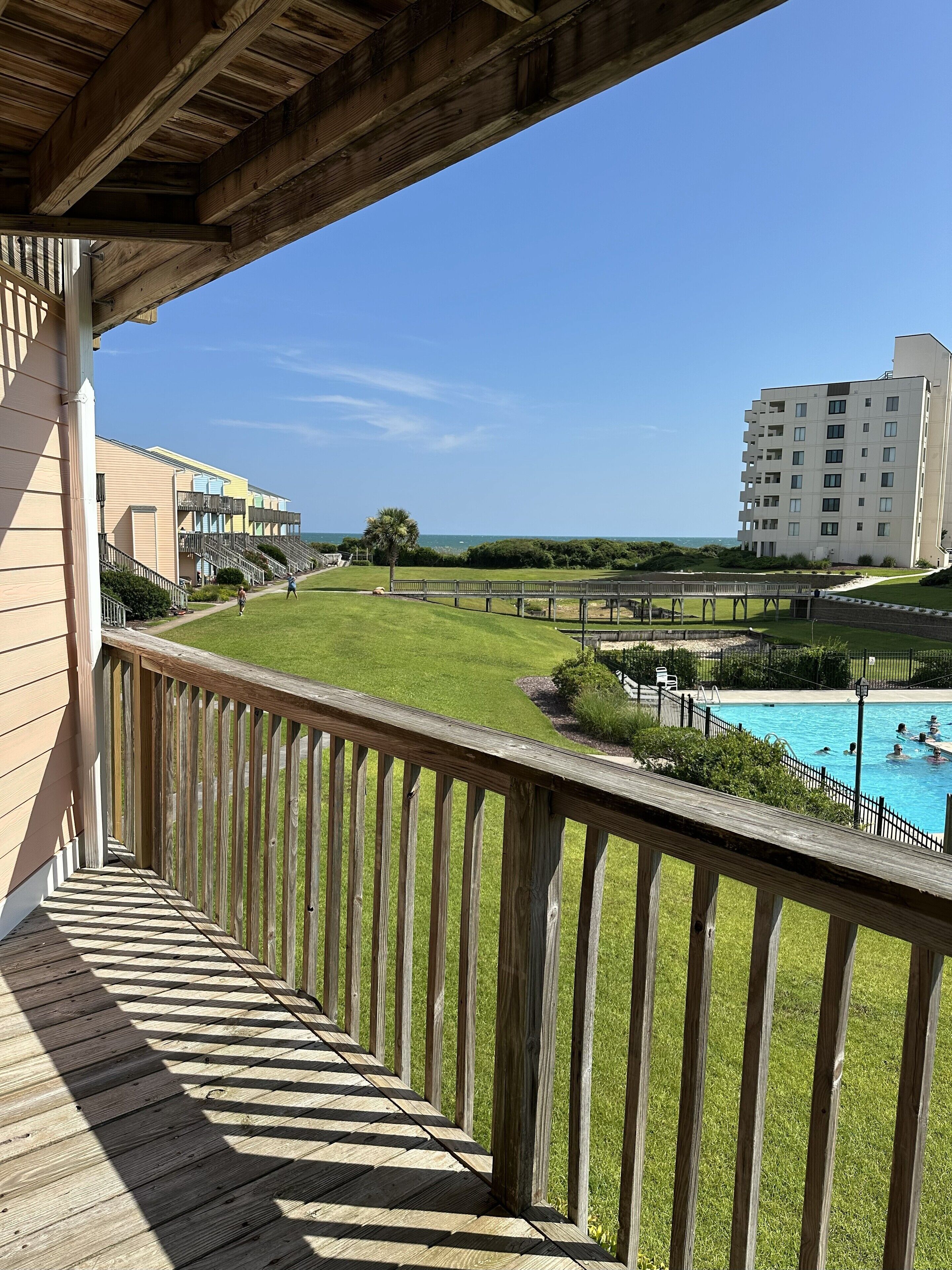 A wooden deck with a view of a swimming pool and a building in the background.
