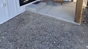 Een overdekt terras met een betonvloer, houten meubilair en een glazen deur naar een binnenruimte.
