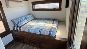 Een kleine slaapkamer met een bed, een raam en een inbouwsbank.