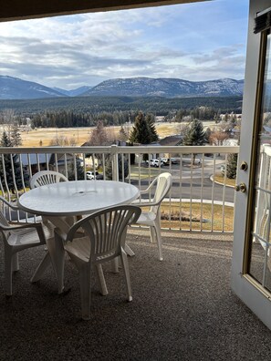 A balcony with a table and chairs, overlooking a snowy mountain range and a residential area. - Cozy getaway with a beautiful view! (Fairmont Hot Springs)