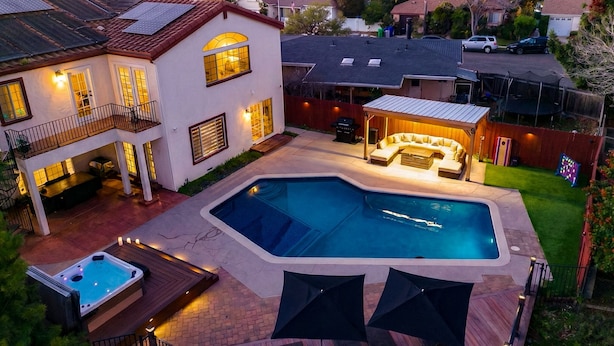 Un cortile residenziale con piscina, vasca idromassaggio e area salotto all'aperto.