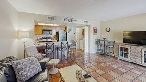 Un salon avec un canapé, une table basse et un téléviseur. Il y a également un coin cuisine équipé d’un réfrigérateur, d’une cuisinière et de chaises.