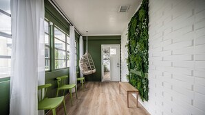 A hallway with green walls, white brick wall with greenery, wooden floor, green chairs, a hanging chair, and a bench. - 2/1 with private backyard in the heart of Ivanhoe (Orlando)