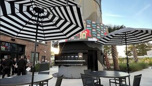 An outdoor patio area with tables and chairs, a large cylindrical structure in the background, and a sign with multiple logos. - 2/1 with private backyard in the heart of Ivanhoe (Orlando)