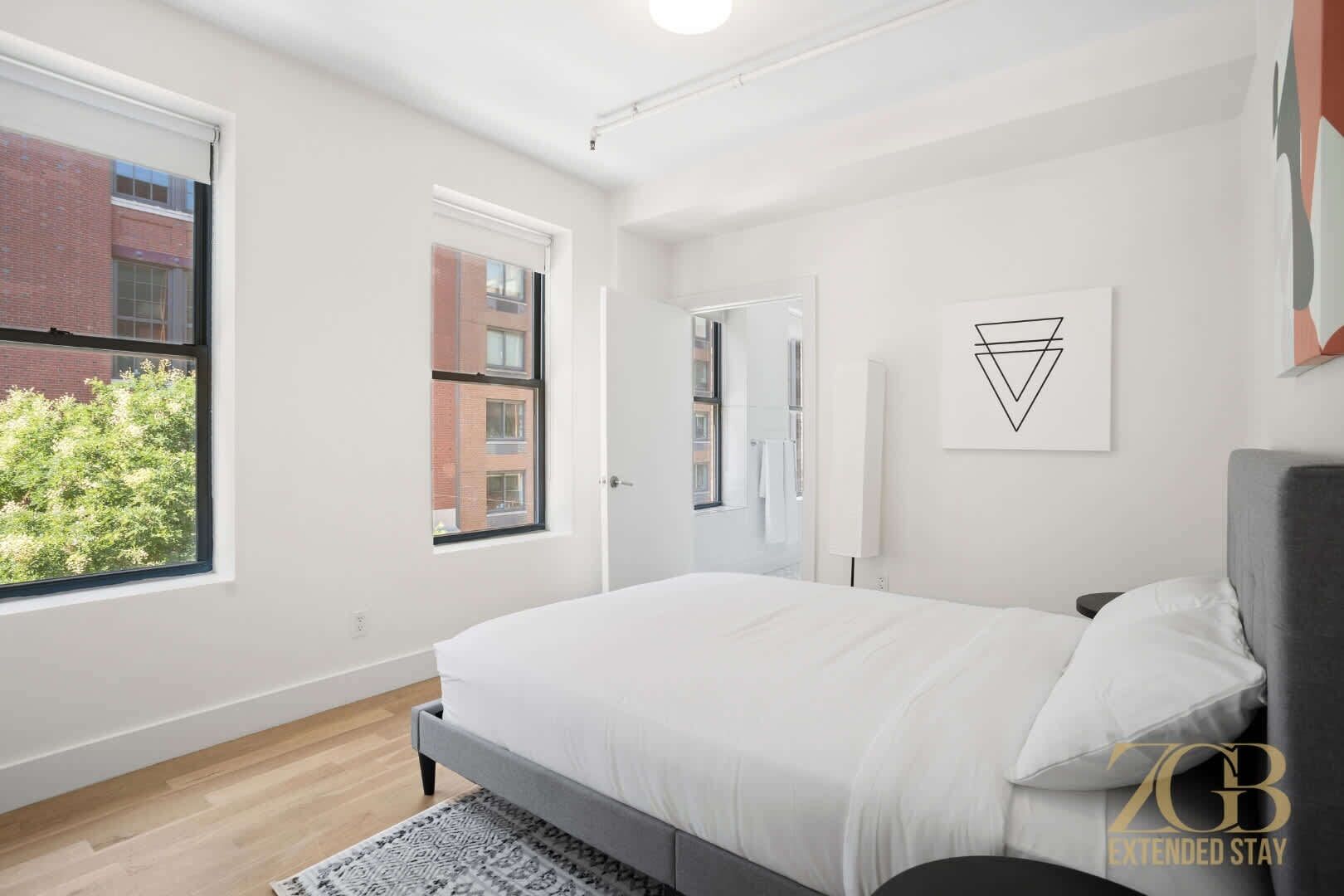 Een moderne slaapkamer met een groot bed, twee ramen en uitzicht op een gebouw van baksteen.