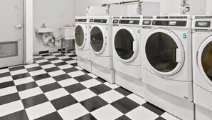 A laundry room with five washing machines, a sink, and a checkered floor. - Renovated 2 Bed 2 Bath Apt in Prime Midtown - Elevator - Laundry (New York)
