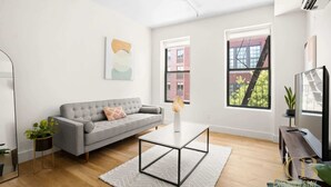 A modern living room with a grey sofa, a coffee table, and a TV. - Renovated 2 Bed 2 Bath Apt in Prime Midtown - Elevator - Laundry (New York)
