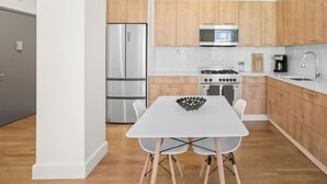 A modern kitchen with wooden cabinets, stainless steel appliances, and a white dining table. - Renovated 2 Bed 2 Bath Apt in Prime Midtown - Elevator - Laundry (New York)