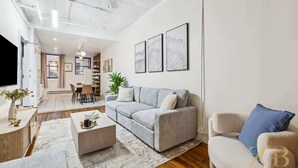 A modern living room with a grey sofa, a white armchair, and a coffee table. There is a dining area in the background with a table and chairs. - Spacious 3BR Flex 4 with Washer & Dryer in NoMad (New York)