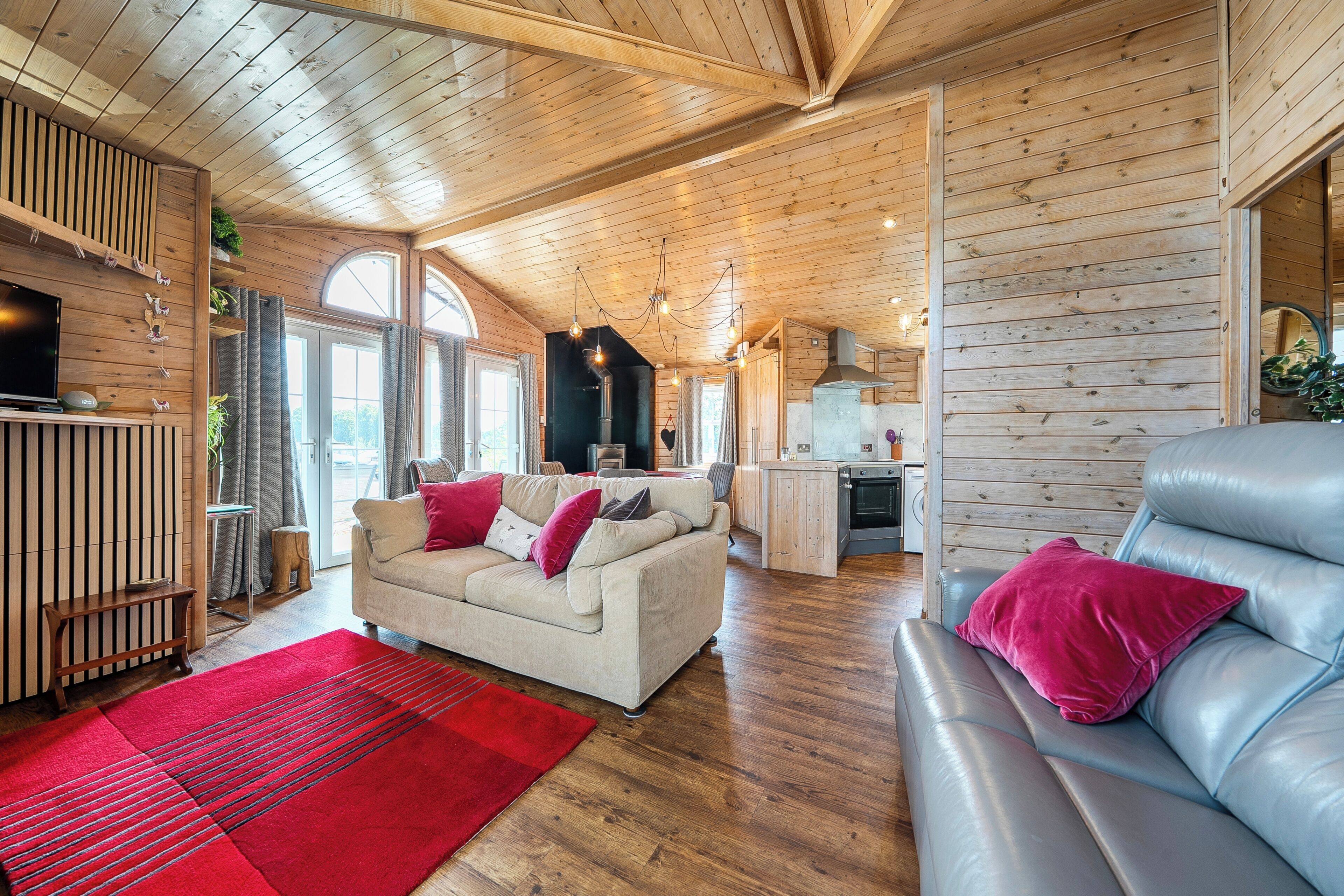 A wooden interior with a sofa, a red rug, and a kitchen area.
