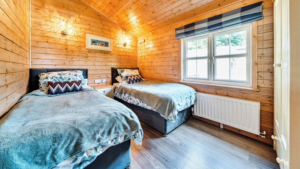 Une chambre de style cabane avec des murs et des planchers en bois, deux lits avec une literie assortie, une fenêtre donnant sur un paysage agréable et un luminaire fixé au mur.