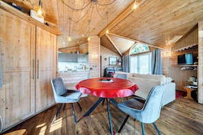 L’intérieur chaleureux d’un chalet, avec un revêtement mural en bois, une table ronde entourée de chaises, un canapé et un téléviseur.