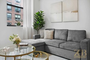 Una sala de estar moderna con un sofá seccional gris, una mesa de centro de vidrio y un ventanal con cortinas.