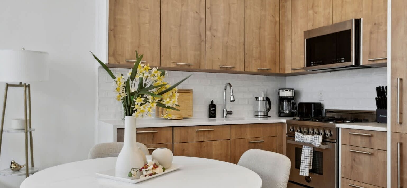 Una cocina moderna con armarios de madera, encimera blanca y comedor con mesa y sillas blancas.