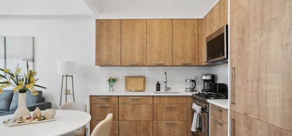 Una cocina moderna con armarios de madera, encimera blanca y comedor con mesa y sillas.