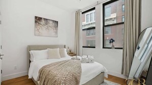 Een moderne hotelkamer met een groot bed, een raam met gordijnen, een schilderij aan de muur en een uitzicht op gebouwen.