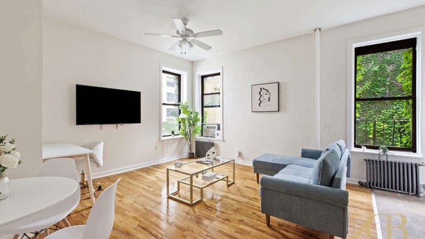 Una sala de estar moderna con un televisor de pantalla plana, un sofá gris, una mesa de centro y un comedor con una mesa y sillas blancas.