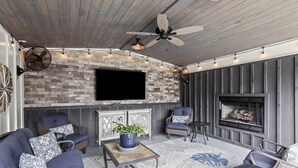 A cozy outdoor living area with a stone wall, a flat-screen TV, and a fireplace. - 5 Minutes from Lake / Cozy Mountain Home with a Heated Pool & Pool House! (Grant)