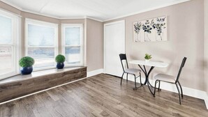 Une pièce avec une baie vitrée, une table blanche avec des chaises et une porte.