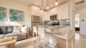 A modern kitchen with white cabinetry, a central island with bar stools, and a built-in microwave. - Beach Paradise 1 Bedroom with Pull Out Sofa (West Bay)