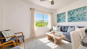 A living room with a sofa, armchairs, a coffee table, and a large window with curtains. - Beach Paradise 1 Bedroom with Pull Out Sofa (West Bay)