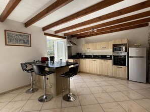 A modern kitchen with wooden beams, a central island with bar stools, and a view to the outside. - Spacious house close to mountains and beaches (Bidarray)