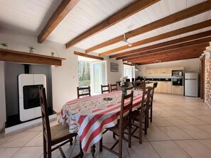 A dining area with a table set for six, wooden chairs, a white ceiling with exposed beams, and a kitchen in the background. - Spacious house close to mountains and beaches (Bidarray)