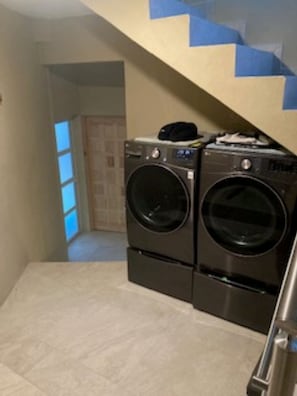 A laundry room with two front-loading washing machines, a tiled floor, and a staircase with blue steps. - Villa Upper Deck!  (Cabo San Lucas)