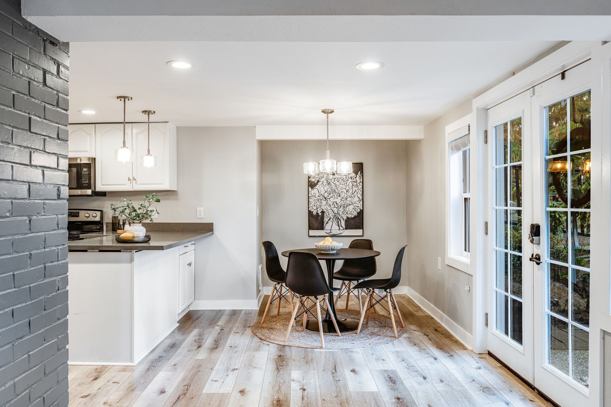 A modern kitchen with white cabinets, a brick accent wall, and a dining area with a round table and chairs.