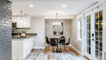 A modern kitchen with white cabinets, a brick accent wall, and a dining area with a round table and chairs.
