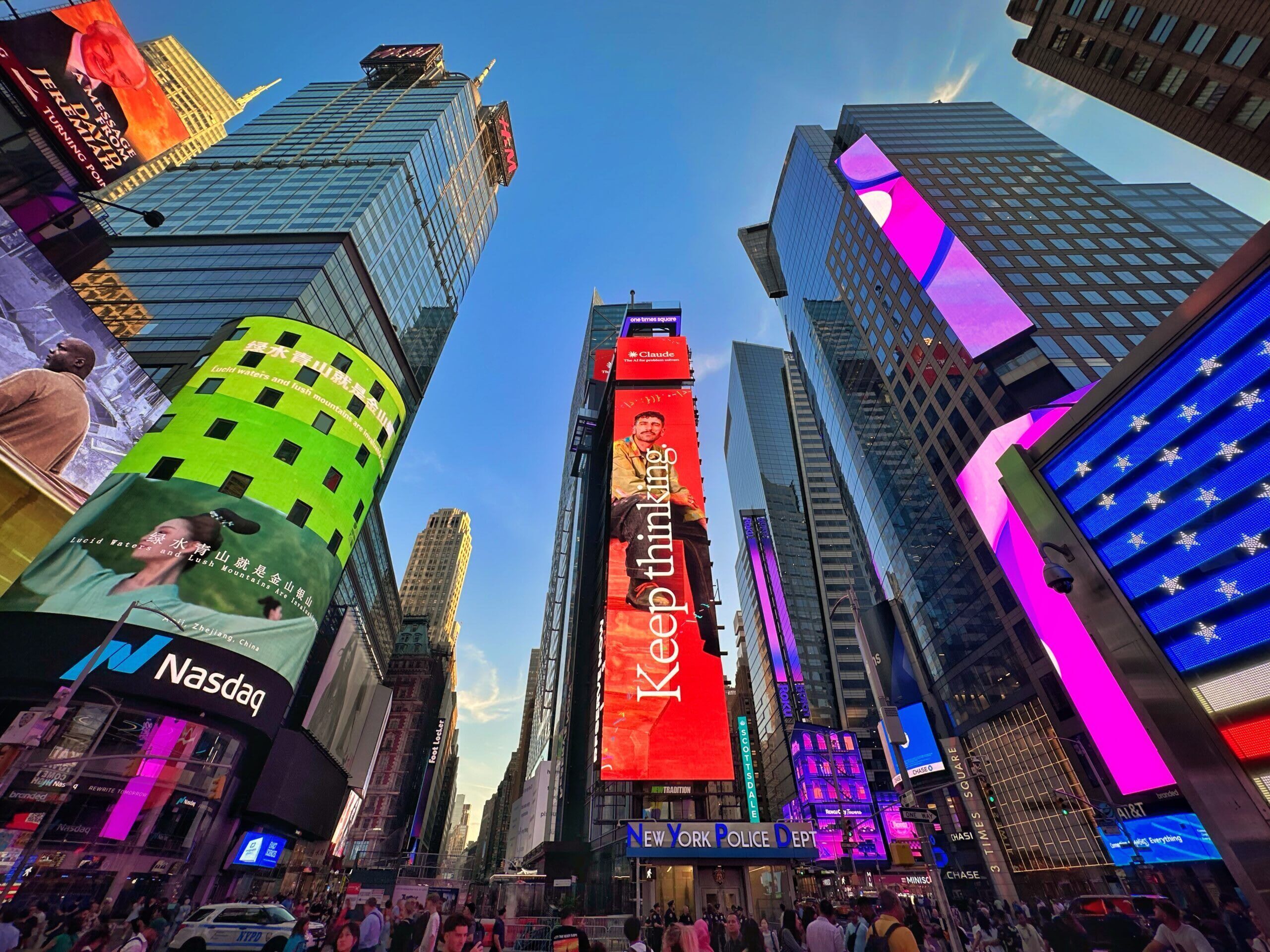 A busy urban street with tall buildings, including a prominent red billboard with the text "Keep thinking."