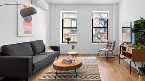 Ein modernes Wohnzimmer mit einer grauen Couch, einem runden Holztisch, einem Sessel und einer TV-Konsole mit einer Pflanze.