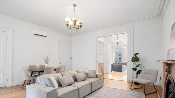 Uma sala de estar moderna com um sofá bege, uma mesa de jantar com cadeiras, um candelabro e uma lareira.