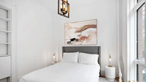 Quarto moderno com cama grande, um quadro acima da cama e uma janela à direita.
