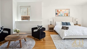 A modern bedroom with a large bed, two nightstands, a wooden coffee table, and two chairs. - Fully Furnished PH Duplex with Private Outdoor Space (New York)