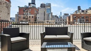 A rooftop terrace with wicker furniture and a glass table, overlooking a cityscape with various buildings. - Fully Furnished PH Duplex with Private Outdoor Space (New York)