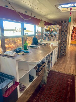 Ein Zimmer mit einem Holztisch, einem Ventilator, einem Fenster mit Aussicht, einer Wand mit Muster und einem roten Teppich.