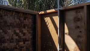 Eine Holzkonstruktion mit einem gewobenen Bambuszaun, einer Metallstange und zwei Flaschen auf einem Regal.