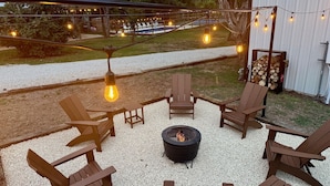 Une terrasse avec des chaises en bois, un foyer et des guirlandes lumineuses.