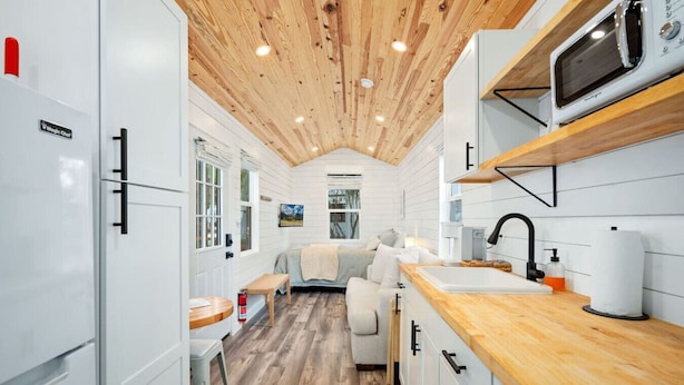 Une cuisine moderne et compacte, avec un plafond en bois, des meubles blancs et un four à micro-ondes.