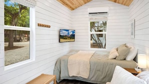 Une chambre confortable dans un chalet, avec un lit, un banc, une télévision et une fenêtre donnant sur la forêt.