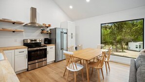 Une cuisine moderne avec un coin repas, des meubles en bois, des appareils électroménagers en acier inoxydable et une grande fenêtre donnant sur un paysage verdoyant.