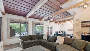 A cozy living room with a sectional sofa, large windows, and a wooden ceiling. - Guadalupe Riverfront | Private Hot Tub | Sleeps 14 (New Braunfels)