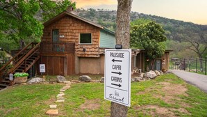 A rustic cabin with a wooden exterior, a staircase, and a signpost indicating directions to 'Palisade', 'Capri', 'Cabins', and 'Fernweh'. - Guadalupe Riverfront | Private Hot Tub | Sleeps 14 (New Braunfels)