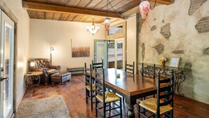 A dining area with a wooden table and chairs, a leather sofa, and a chandelier. - Guadalupe Riverfront | Private Hot Tub | Sleeps 14 (New Braunfels)