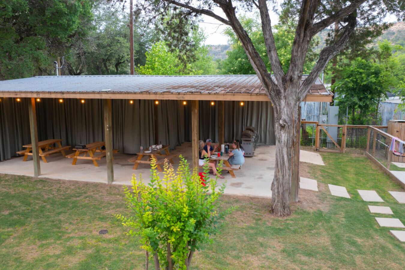 Un espace extérieur abrité avec des tables de pique-nique, un arbre et une cour clôturée.