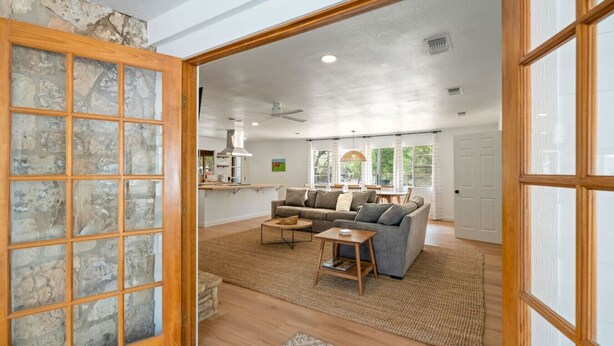 An open-plan living area with a stone wall, a sofa set, a coffee table, and a kitchen in the background. - Guadalupe Cabins | 3 Cottages | Sleeps 17-23 (New Braunfels)