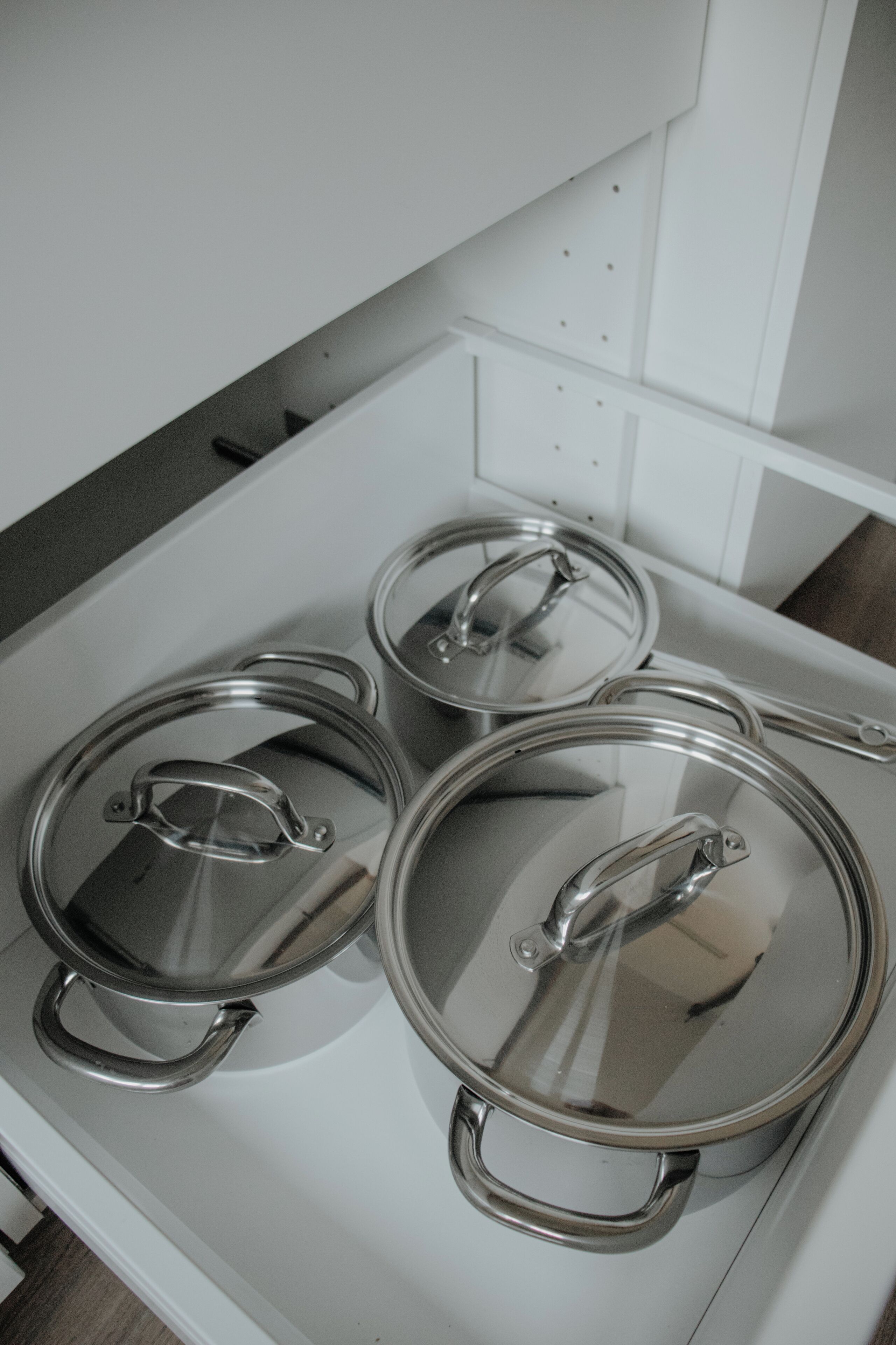 Trois casseroles en acier inoxydable, avec leurs couvercles, sur une cuisinière blanche.