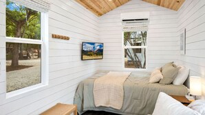 A cozy bedroom with a bed, a TV, and a window overlooking a tree. - Cozy Up with Perfect Private Escape for 2 | Pool + River (New Braunfels)